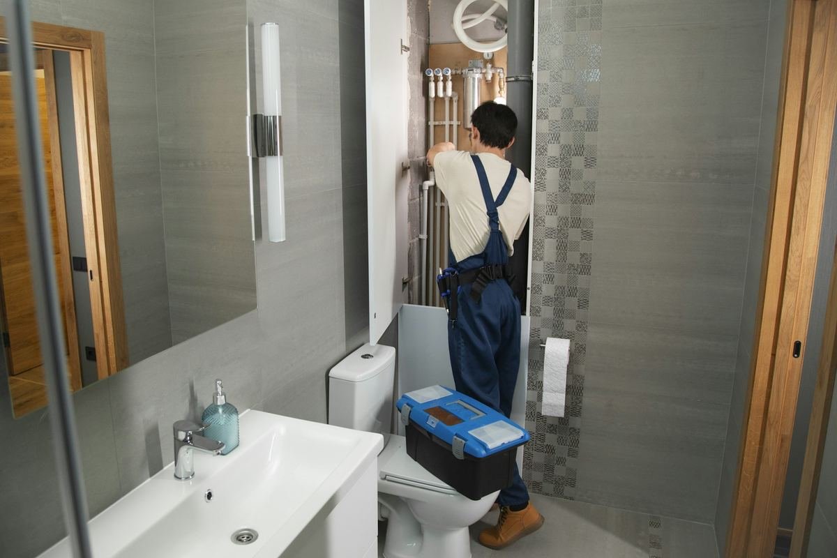 Plumber working on pipes in a bathroom wall